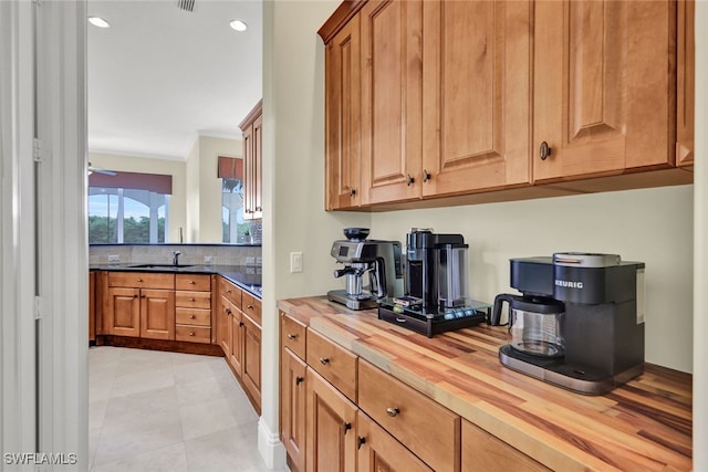 kitchen with butcher block countertops, light tile patterned floors, sink, and ornamental molding