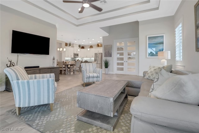 living room featuring light wood-type flooring, ceiling fan with notable chandelier, and a raised ceiling