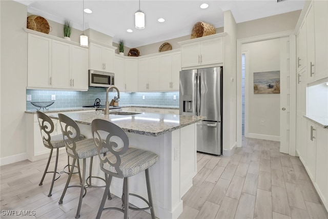 kitchen with stainless steel appliances, pendant lighting, light stone countertops, an island with sink, and white cabinets