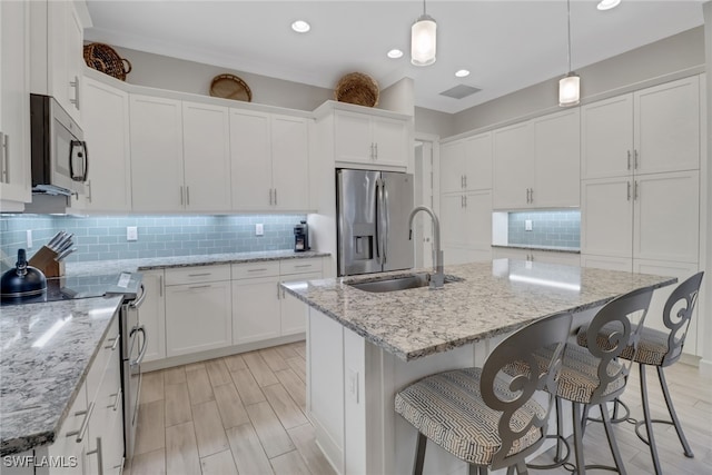 kitchen featuring stainless steel appliances, hanging light fixtures, white cabinetry, and an island with sink