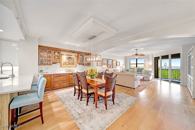 dining area with light hardwood / wood-style floors, ceiling fan with notable chandelier, sink, and crown molding