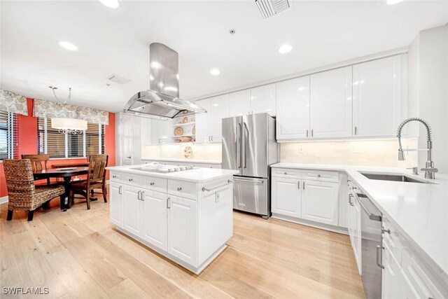 kitchen featuring sink, light wood-type flooring, stainless steel appliances, island exhaust hood, and white cabinets