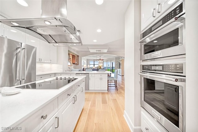 kitchen featuring appliances with stainless steel finishes, island range hood, light wood-type flooring, white cabinetry, and kitchen peninsula