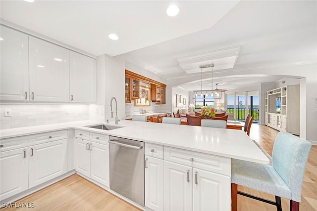 kitchen featuring sink, white cabinetry, stainless steel dishwasher, kitchen peninsula, and hanging light fixtures