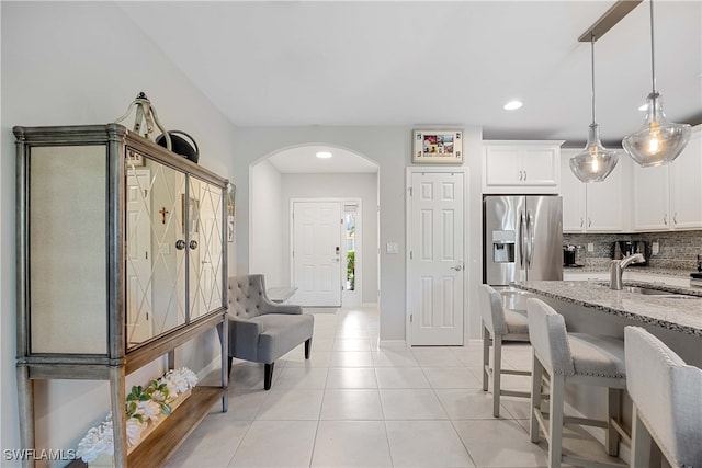 kitchen featuring backsplash, sink, decorative light fixtures, light stone counters, and stainless steel refrigerator with ice dispenser