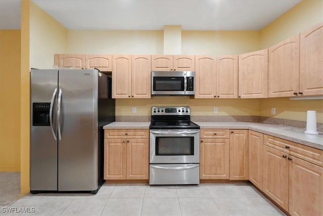 kitchen with light brown cabinetry, light tile patterned floors, appliances with stainless steel finishes, and light stone countertops