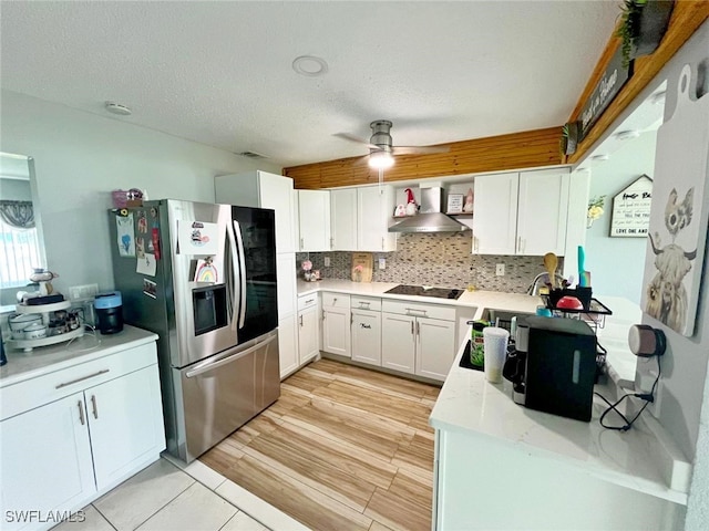 kitchen featuring white cabinets, stainless steel refrigerator with ice dispenser, wall chimney range hood, black electric cooktop, and ceiling fan