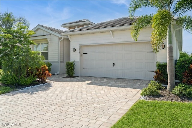 view of front facade featuring an attached garage, a tile roof, and decorative driveway