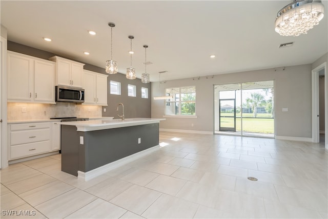 kitchen featuring white cabinets, a kitchen island with sink, light tile patterned flooring, pendant lighting, and tasteful backsplash