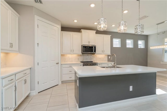 kitchen with tasteful backsplash, a center island with sink, appliances with stainless steel finishes, light countertops, and a sink