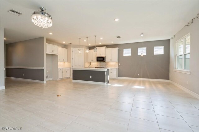 kitchen with an island with sink, pendant lighting, light tile patterned floors, and tasteful backsplash