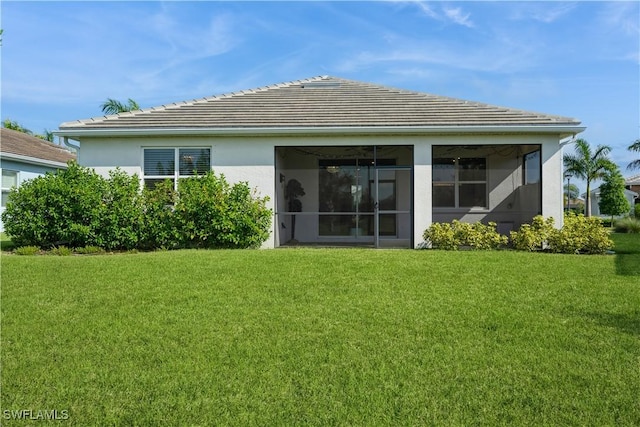 rear view of property with a yard, a tiled roof, a sunroom, and stucco siding