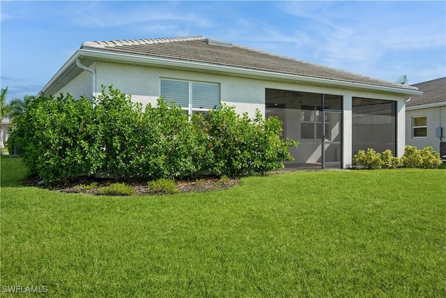 rear view of property with a sunroom, a tile roof, a yard, and stucco siding