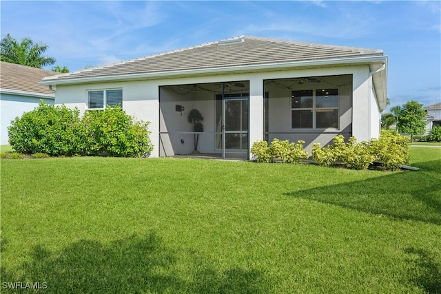 rear view of house featuring a tiled roof, a lawn, a sunroom, and stucco siding