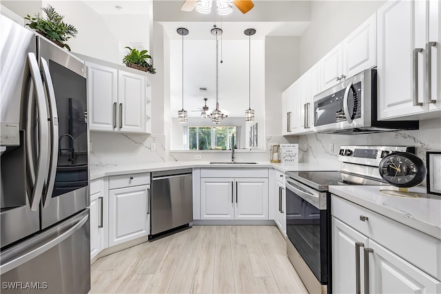 kitchen with appliances with stainless steel finishes, white cabinetry, ceiling fan with notable chandelier, pendant lighting, and light wood-type flooring