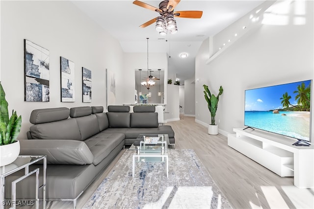 living room featuring high vaulted ceiling, light hardwood / wood-style floors, and ceiling fan with notable chandelier