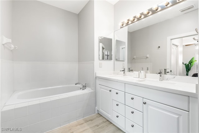 bathroom with ceiling fan, tiled tub, wood-type flooring, and vanity