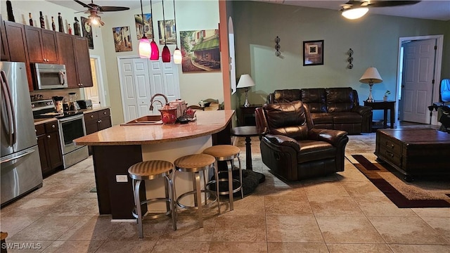 kitchen featuring a kitchen breakfast bar, ceiling fan, an island with sink, decorative light fixtures, and stainless steel appliances