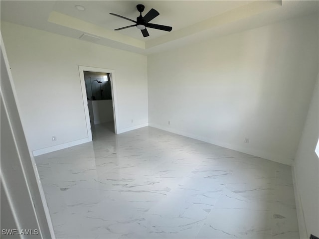 tiled empty room featuring ceiling fan and a raised ceiling