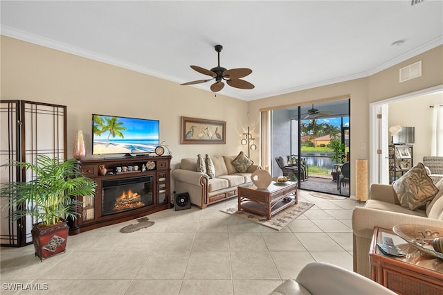 living room featuring light tile patterned floors, visible vents, ornamental molding, a glass covered fireplace, and ceiling fan