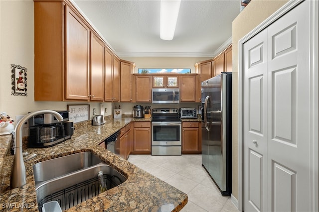 kitchen with light tile patterned floors, dark stone counters, appliances with stainless steel finishes, crown molding, and a sink