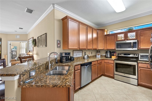 kitchen featuring a peninsula, a sink, appliances with stainless steel finishes, brown cabinetry, and crown molding