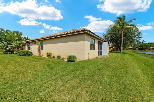 view of side of property featuring a tiled roof, a lawn, and stucco siding