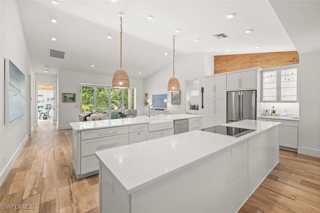 kitchen with light wood-type flooring, appliances with stainless steel finishes, pendant lighting, and a spacious island