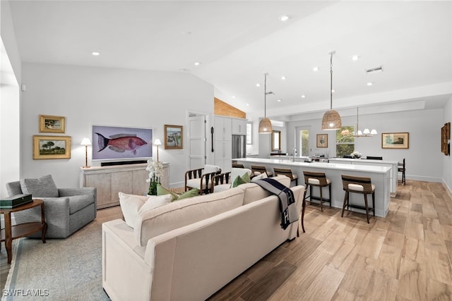 living room featuring light hardwood / wood-style floors, sink, high vaulted ceiling, and a chandelier