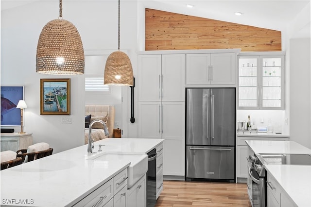 kitchen featuring hanging light fixtures, light hardwood / wood-style flooring, vaulted ceiling, white cabinetry, and stainless steel appliances