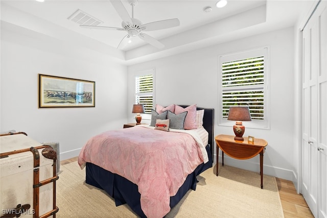 bedroom with light wood-type flooring, a raised ceiling, a closet, and ceiling fan