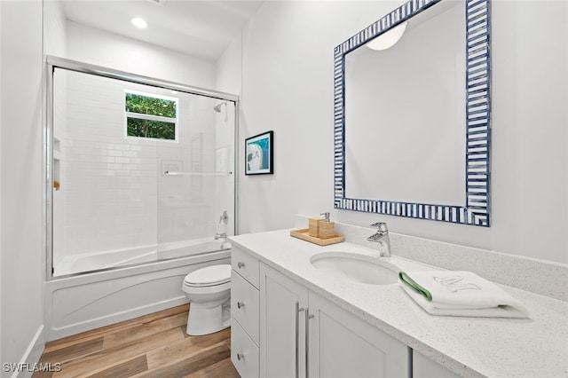 full bathroom with bath / shower combo with glass door, vanity, wood-type flooring, and toilet