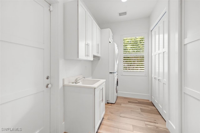 washroom featuring sink, stacked washer and dryer, cabinets, and light wood-type flooring