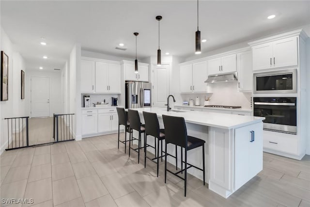 kitchen with stainless steel appliances, decorative light fixtures, a kitchen island with sink, and white cabinets