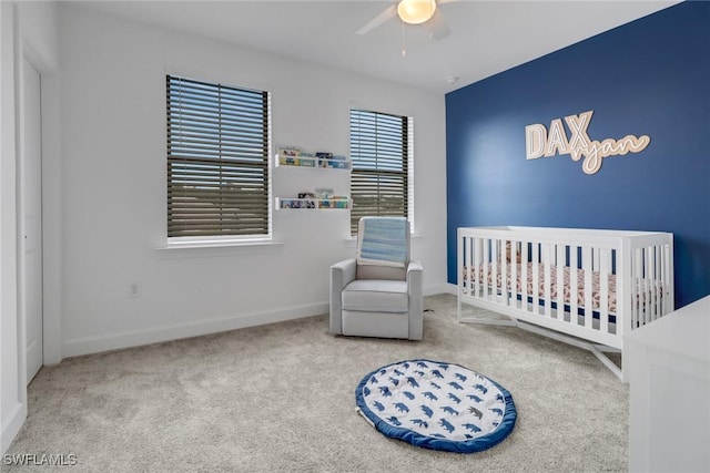 carpeted bedroom featuring a nursery area and ceiling fan