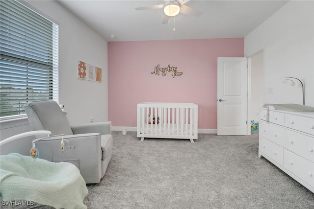 bedroom featuring light colored carpet, a nursery area, and ceiling fan