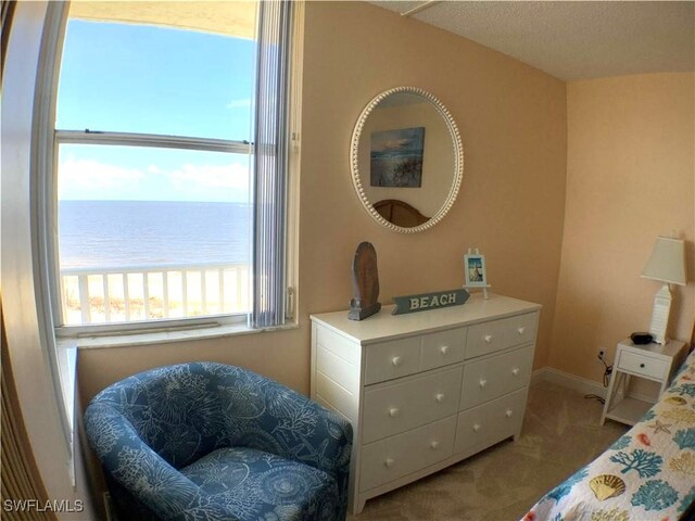 bedroom with a beach view, a water view, light colored carpet, and a textured ceiling