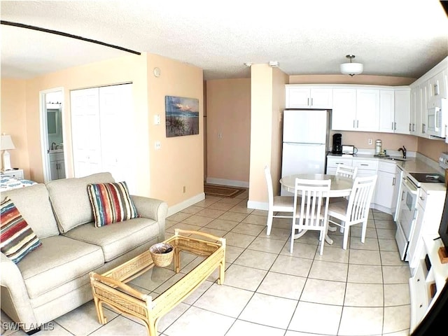 kitchen featuring a textured ceiling, white appliances, sink, light tile patterned floors, and white cabinets