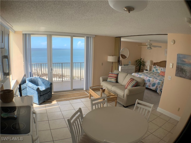 tiled living room with a beach view, a textured ceiling, a water view, and ceiling fan