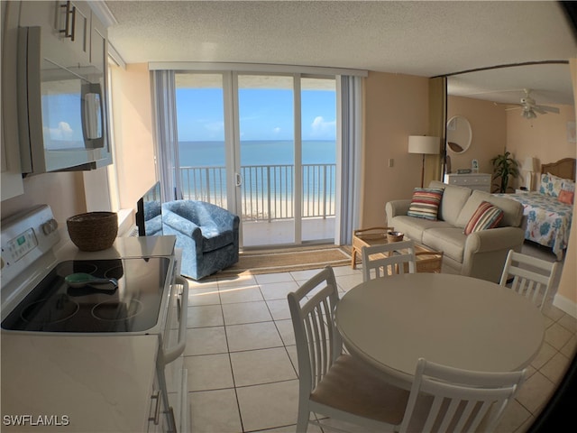 tiled living room with ceiling fan, a water view, and a textured ceiling