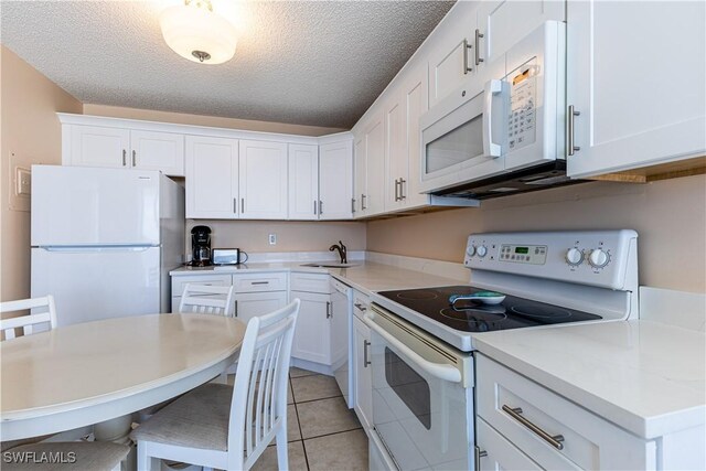 kitchen featuring a textured ceiling, white cabinetry, sink, and white appliances