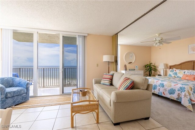 bedroom featuring a water view, ceiling fan, access to exterior, a textured ceiling, and light colored carpet