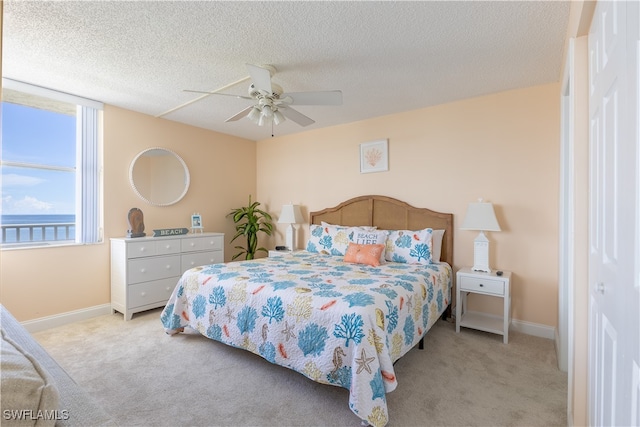 bedroom with ceiling fan, light colored carpet, and a textured ceiling