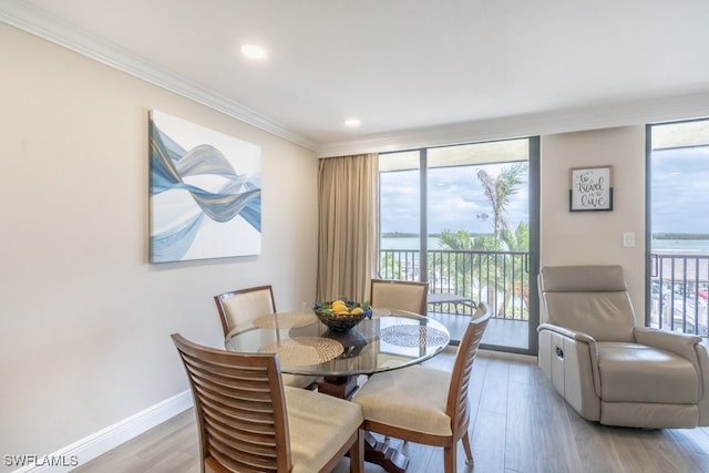 dining space featuring ornamental molding, light hardwood / wood-style floors, a wall of windows, and a water view