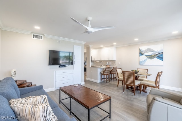 living room featuring ceiling fan, light hardwood / wood-style flooring, sink, and ornamental molding