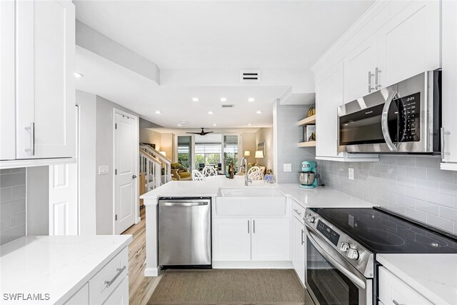 kitchen with light hardwood / wood-style flooring, tasteful backsplash, appliances with stainless steel finishes, sink, and kitchen peninsula