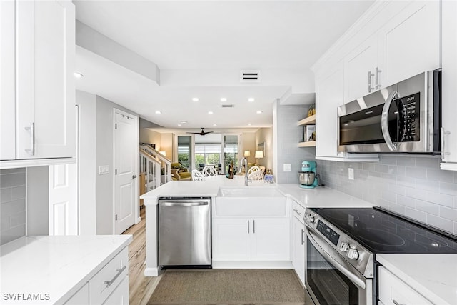 kitchen featuring light stone counters, appliances with stainless steel finishes, white cabinets, a sink, and a peninsula