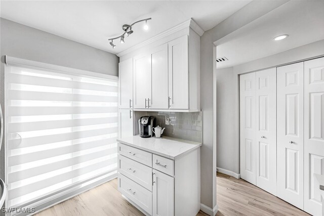 kitchen with rail lighting, tasteful backsplash, light wood-type flooring, light stone countertops, and white cabinets