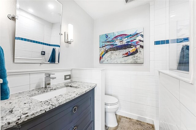 bathroom featuring tiled shower, toilet, vanity, and tile walls