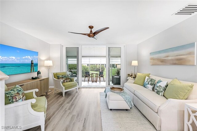 living room with ceiling fan, light hardwood / wood-style flooring, and a wall of windows